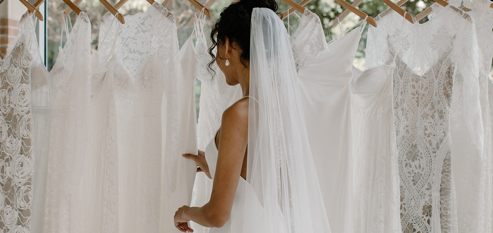 bride wearing wedding dressing looking at dresses hanging on a rail